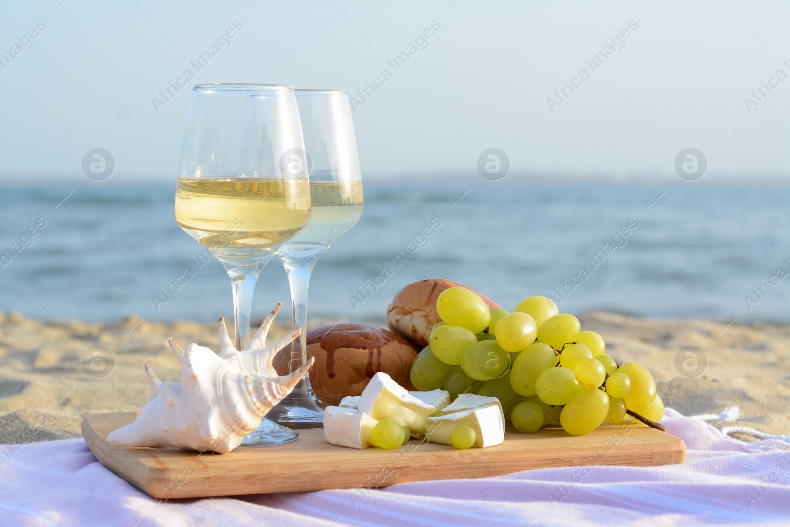 Photo of Glasses with white wine and snacks for beach picnic on sandy seashore