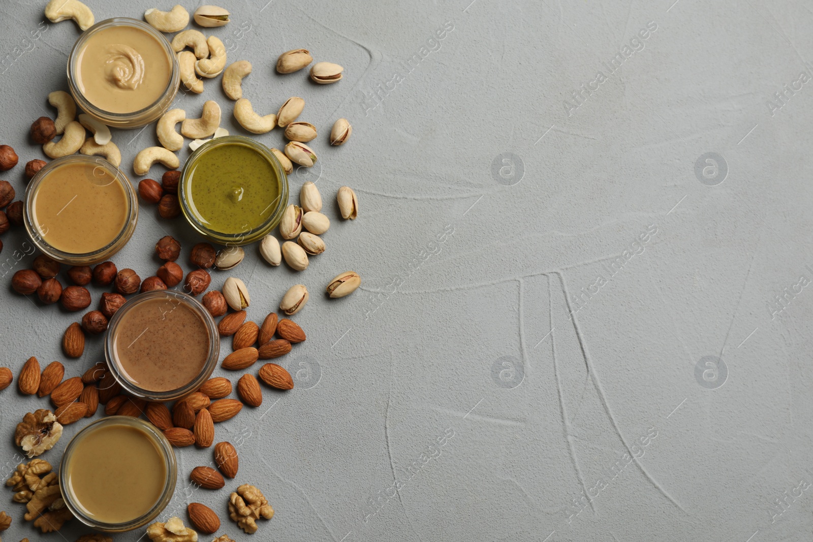 Photo of Jars with butters made of different nuts and ingredients on grey table, flat lay. Space for text