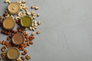 Photo of Jars with butters made of different nuts and ingredients on grey table, flat lay. Space for text