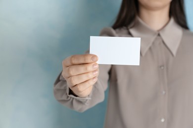 Photo of Woman holding blank business card on light blue background, closeup. Mockup for design