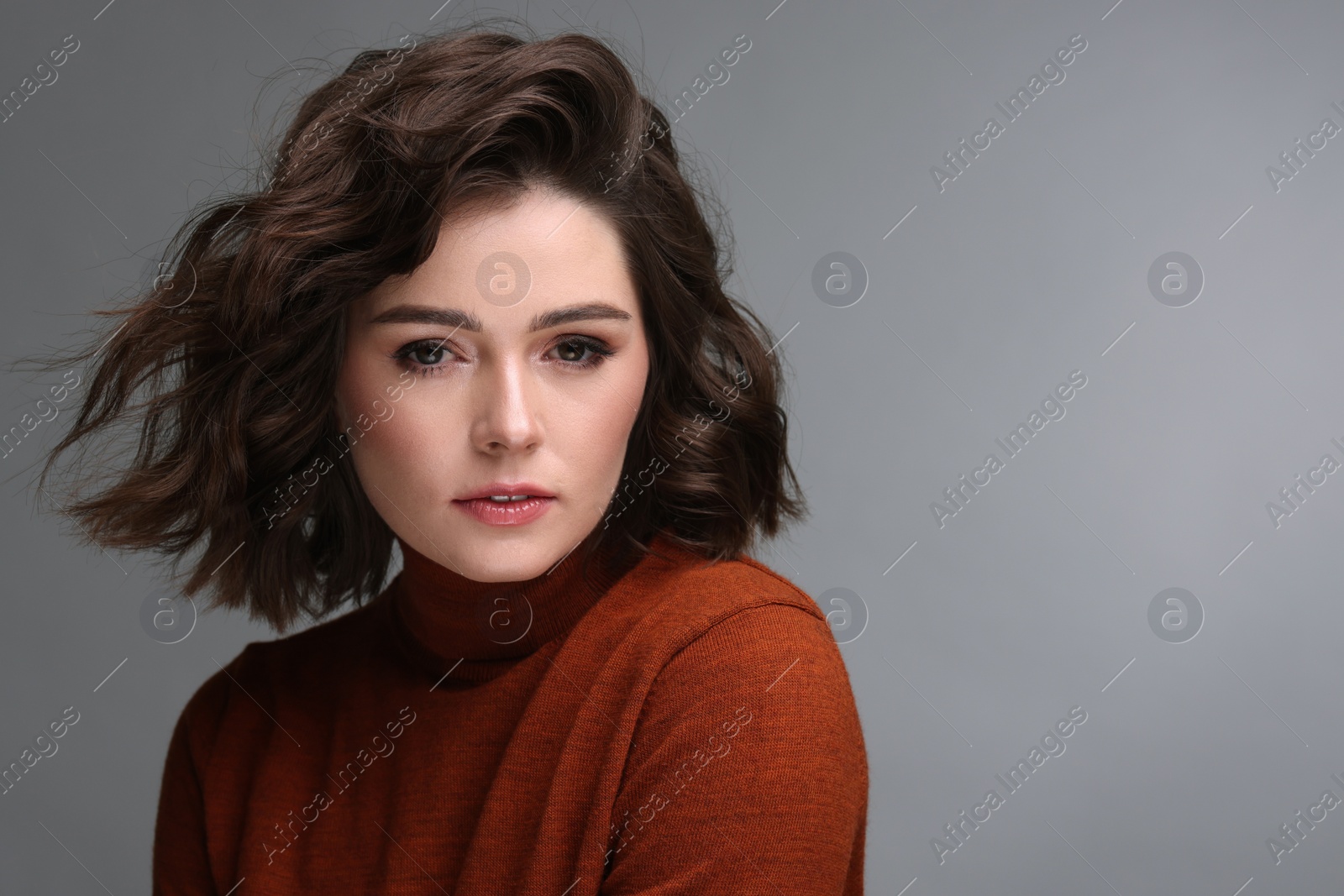 Photo of Portrait of beautiful young woman with wavy hairstyle on grey background. Space for text