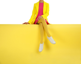 Woman wearing yellow tights and stylish shoes sitting on color background, closeup