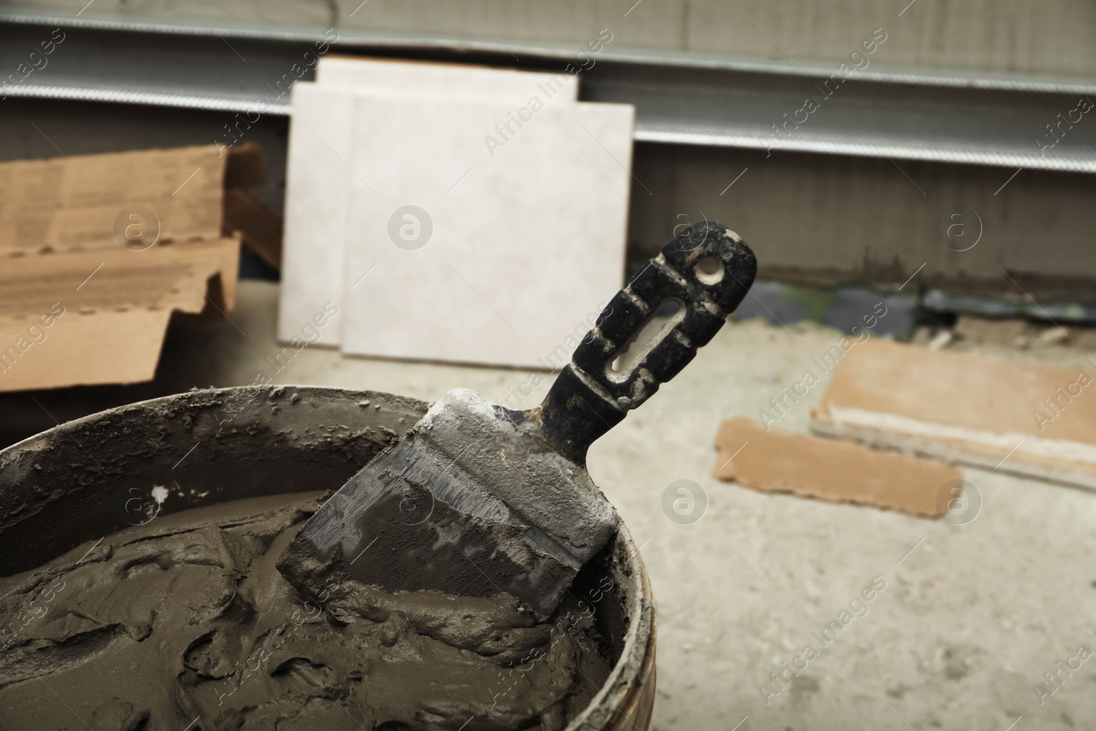 Photo of Adhesive mix, spatula and ceramic tiles on floor, closeup