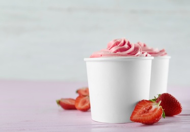 Cups with tasty frozen yogurt and strawberries on pink wooden table. Space for text