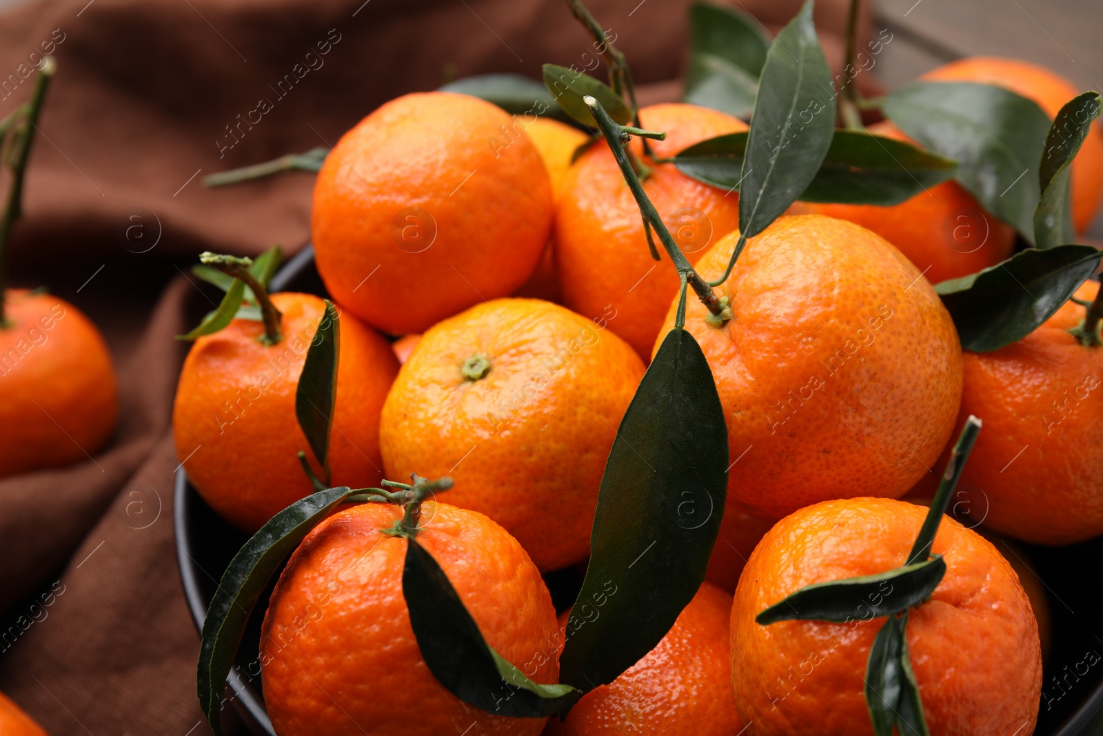 Photo of Fresh ripe tangerines with green leaves in bowl on table, closeup