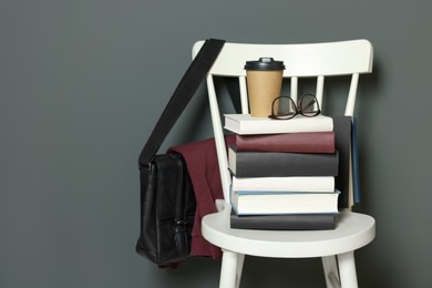 Stack of different books, paper cup and glasses on white chair. Space for text