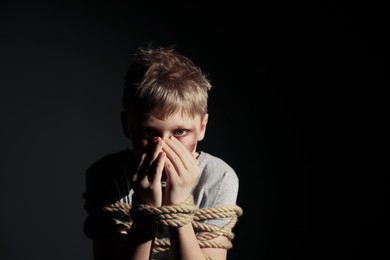 Little boy with bruises tied up and taken hostage on dark background. Space for text