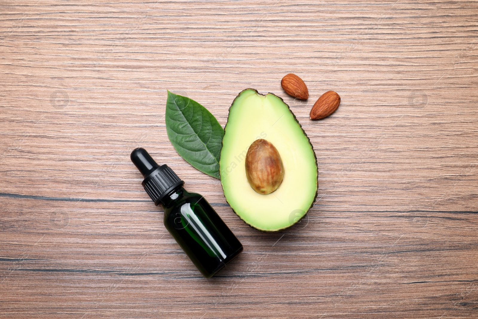 Photo of Bottle of essential oil, fresh avocado and almonds on wooden table, flat lay