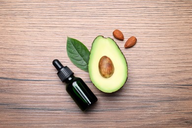 Bottle of essential oil, fresh avocado and almonds on wooden table, flat lay