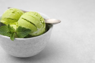 Photo of Tasty matcha ice cream and spoon in bowl on light grey table, closeup. Space for text