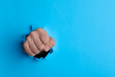 Man breaking through light blue paper with fist, closeup. Space for text