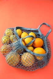String bag with oranges and lemons on red background, top view