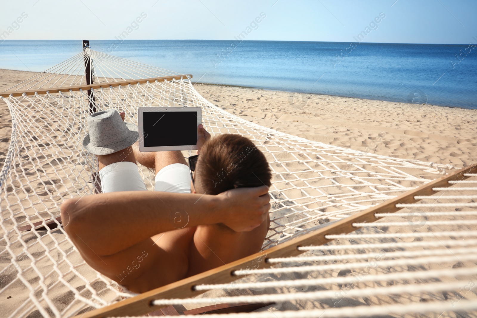 Photo of Young man with tablet in hammock on beach