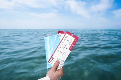 Image of Man holding tickets and protective mask outdoors, closeup. Travel during quarantine