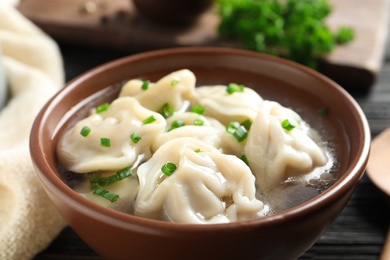 Photo of Bowl of tasty dumplings in broth on table, closeup