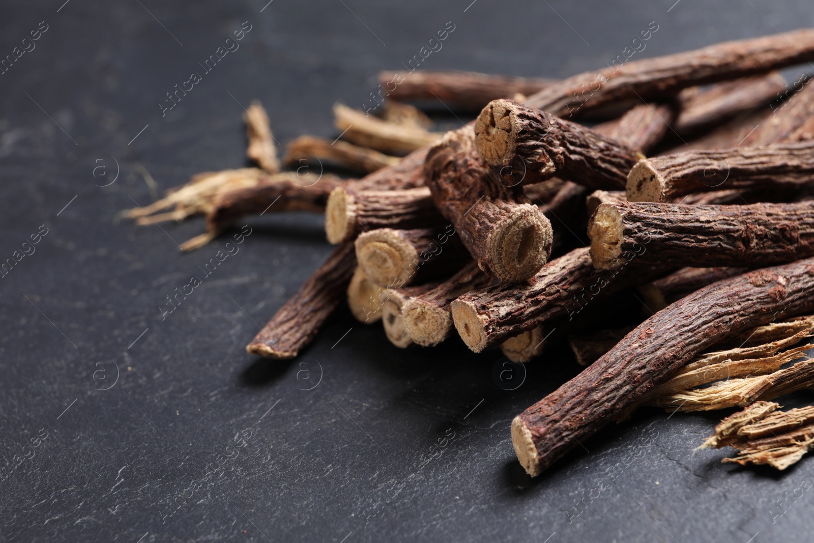 Photo of Dried sticks of liquorice root on black table, closeup. Space for text