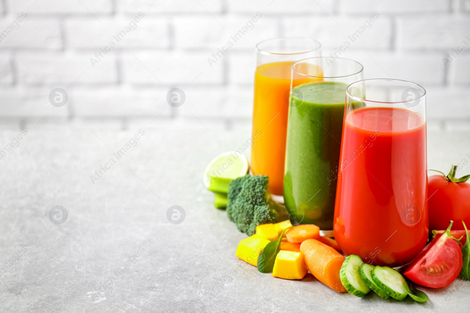 Photo of Different tasty juices and fresh ingredients on grey table against brick wall. Space for text