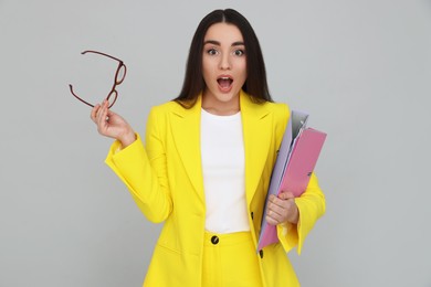 Young female intern with eyeglasses and folders on grey background