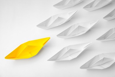 Group of paper boats following yellow one on white background, flat lay. Leadership concept