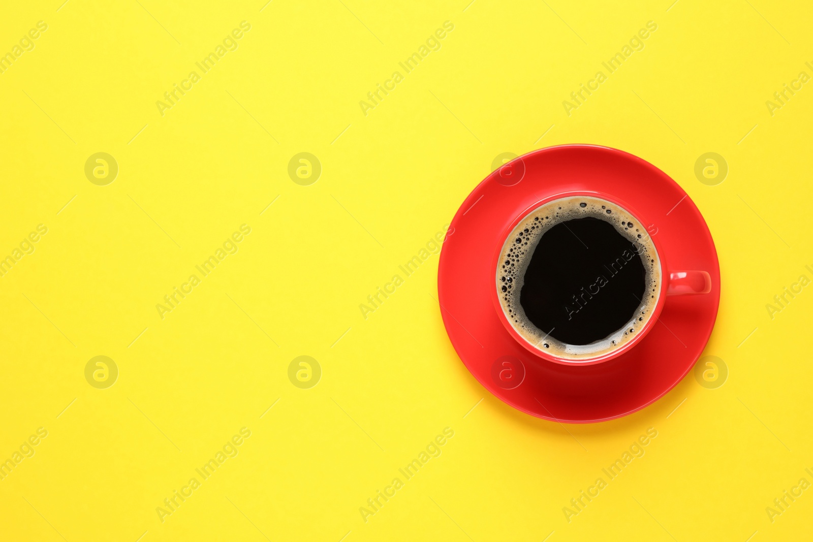 Photo of Aromatic coffee in red cup on yellow background, top view. Space for text