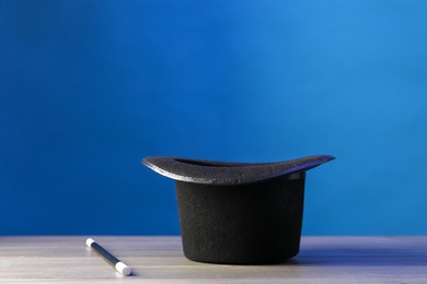 Photo of Magician's hat and wand on wooden table against blue background, space for text