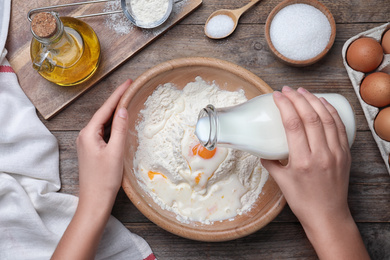 Photo of Woman preparing batter for thin pancakes at wooden table, top view