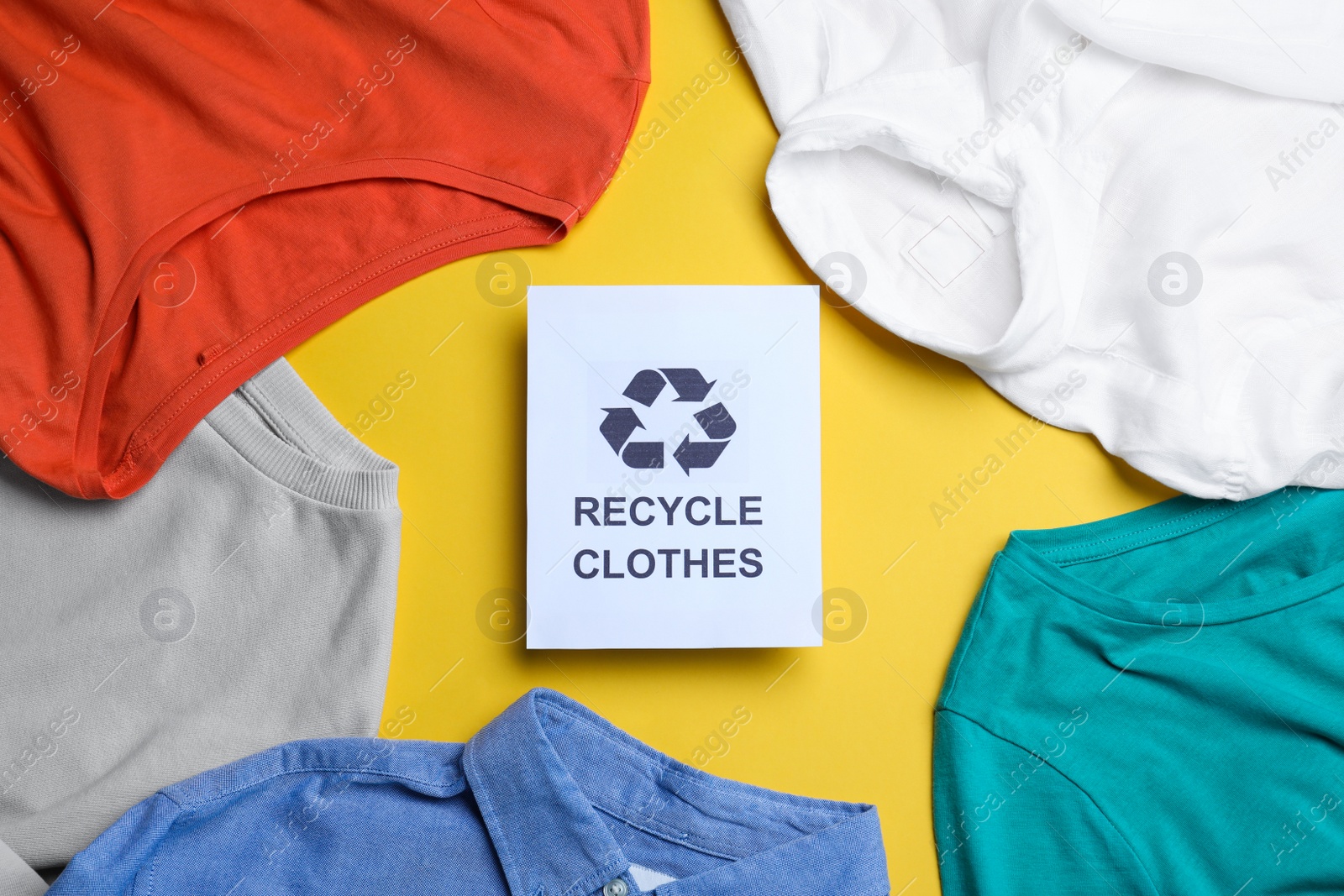 Photo of Different clothes with recycling label on yellow background, flat lay