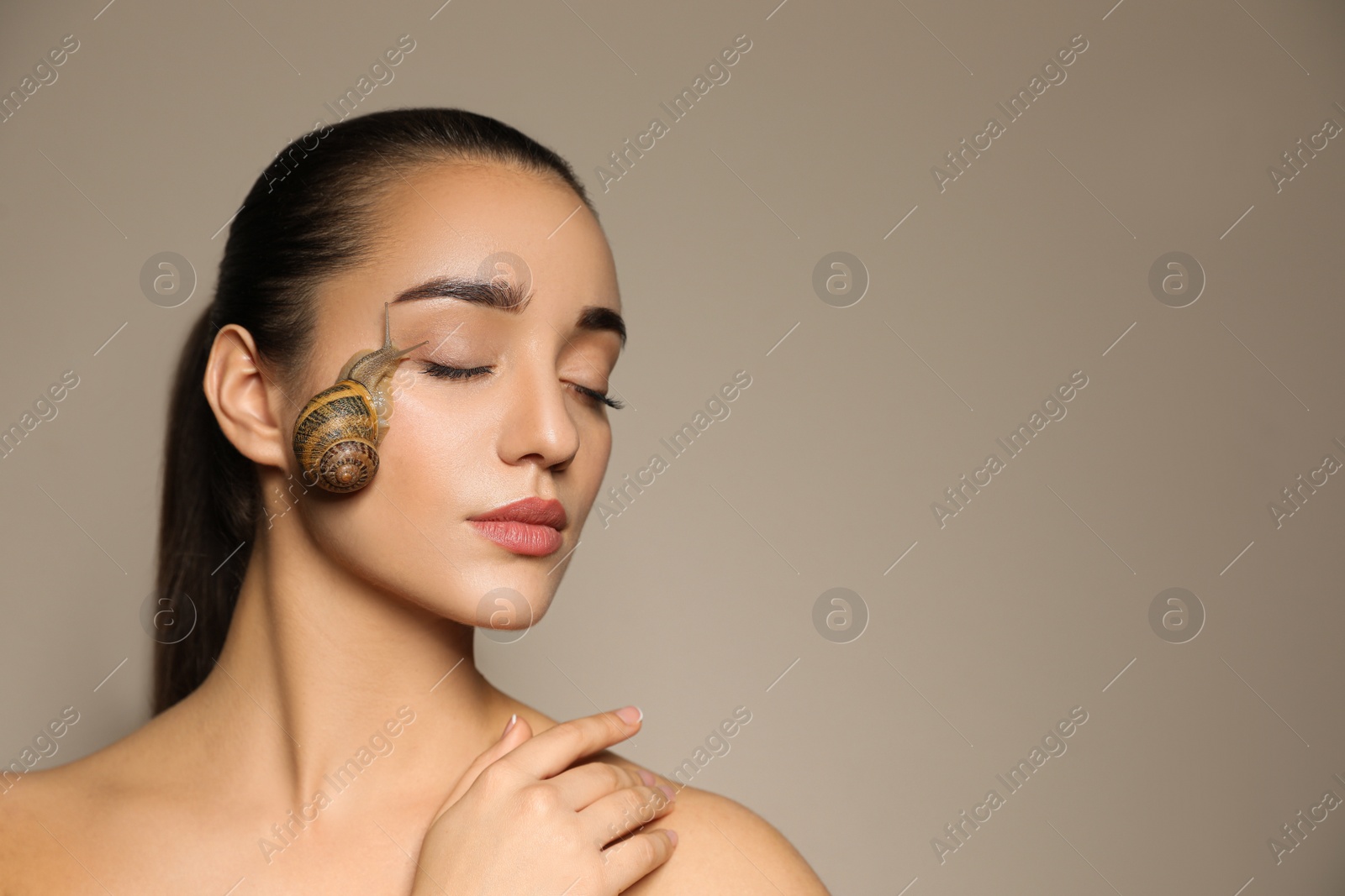 Photo of Beautiful young woman with snail on her face against beige background. Space for text