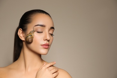 Beautiful young woman with snail on her face against beige background. Space for text