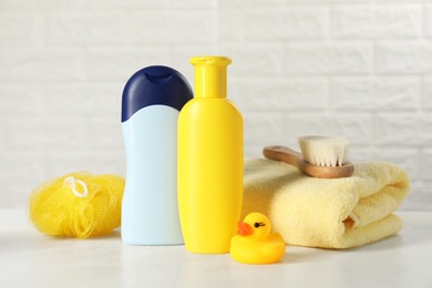 Photo of Baby cosmetic products, bath duck, brush and towel on white table against brick wall