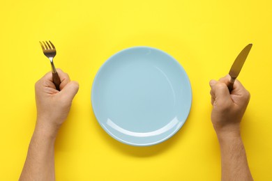 Photo of Man with fork, knife and empty plate at yellow table, top view