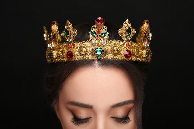 Beautiful young woman wearing luxurious crown on black background, closeup