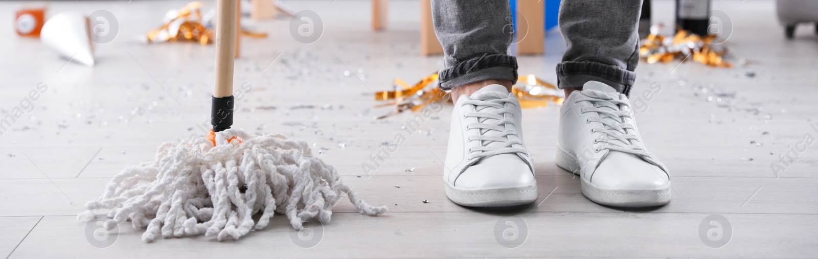 Image of Young man with mop cleaning messy room after party, closeup of legs. Banner design