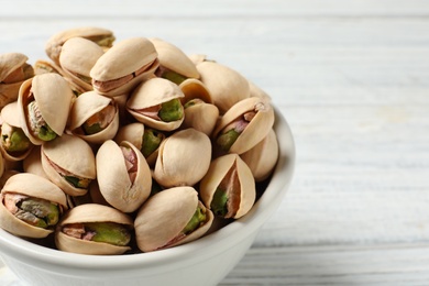 Photo of Organic pistachio nuts in bowl on wooden table, closeup. Space for text