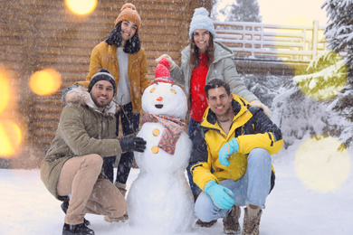 Photo of Happy friends near snowman outdoors on snowy day. Winter vacation