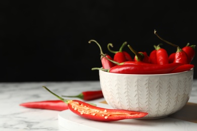 Photo of Bowl with red hot chili peppers and cut one on marble table. Space for text