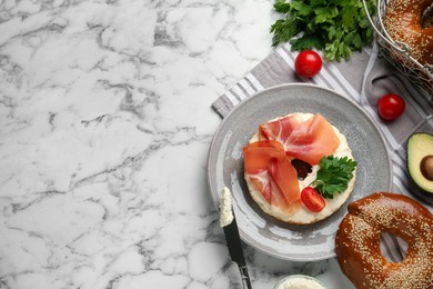 Photo of Delicious bagel with cream cheese, jamon, tomato and parsley on white marble table, flat lay. Space for text