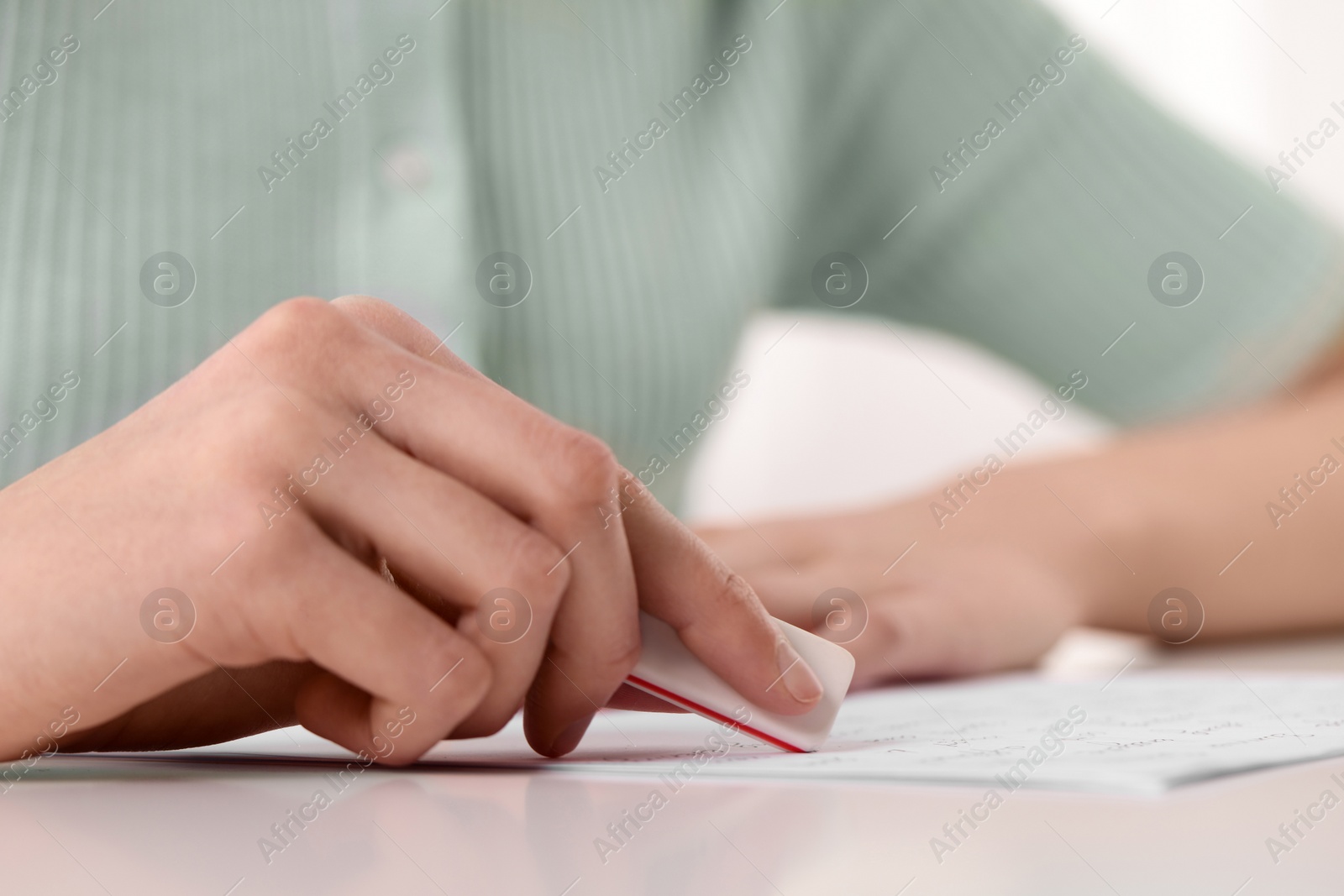 Photo of Girl erasing mistake in her notebook at white desk, closeup