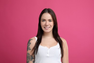 Photo of Beautiful woman with tattoos on arm against pink background