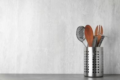 Photo of Holder with kitchen utensils on grey table against light background. Space for text