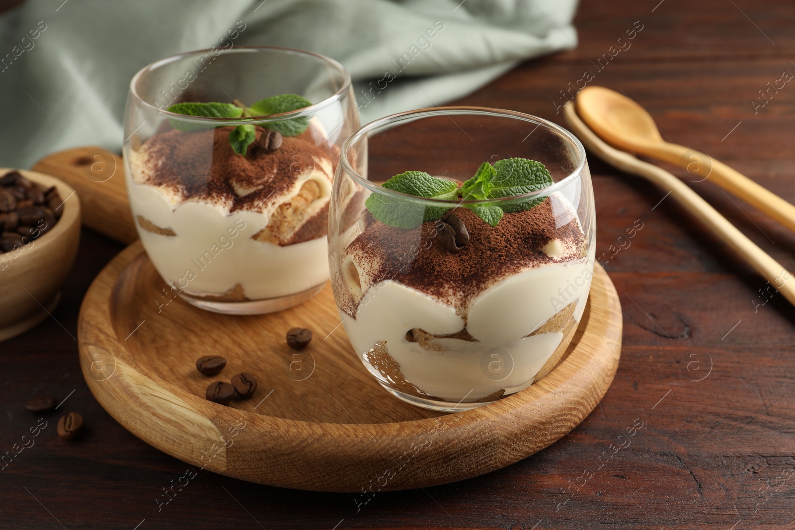 Photo of Delicious tiramisu in glasses, mint leaves and coffee beans on wooden table