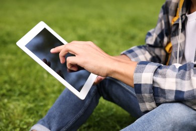 Photo of Student studying with tablet on green grass in park, closeup