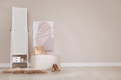 Photo of Stylish pouf and mirror near beige wall indoors. Space for text