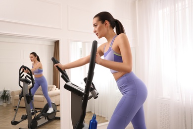 Woman using modern elliptical machine at home