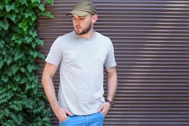 Photo of Young man wearing gray t-shirt near wall on street. Urban style