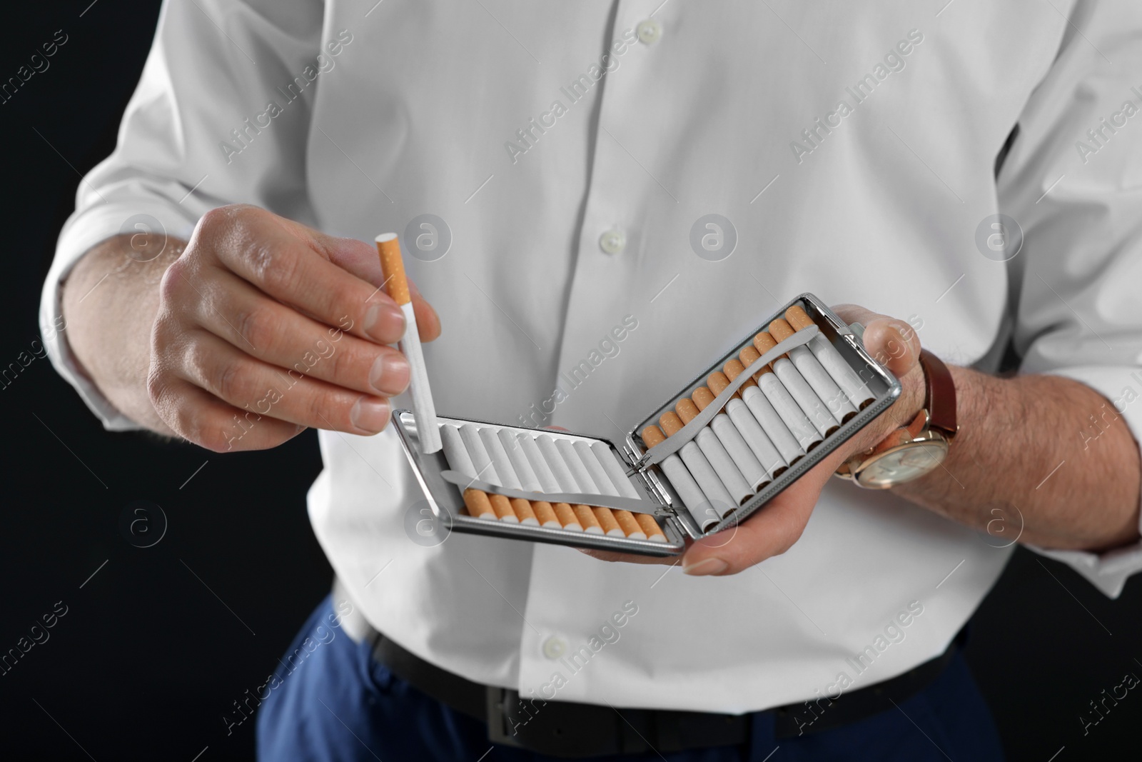 Photo of Man taking cigarette from holder on black background, closeup