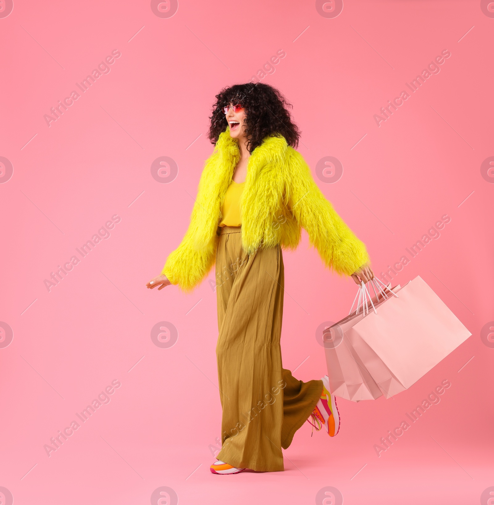 Photo of Happy young woman with shopping bags on pink background. Space for text