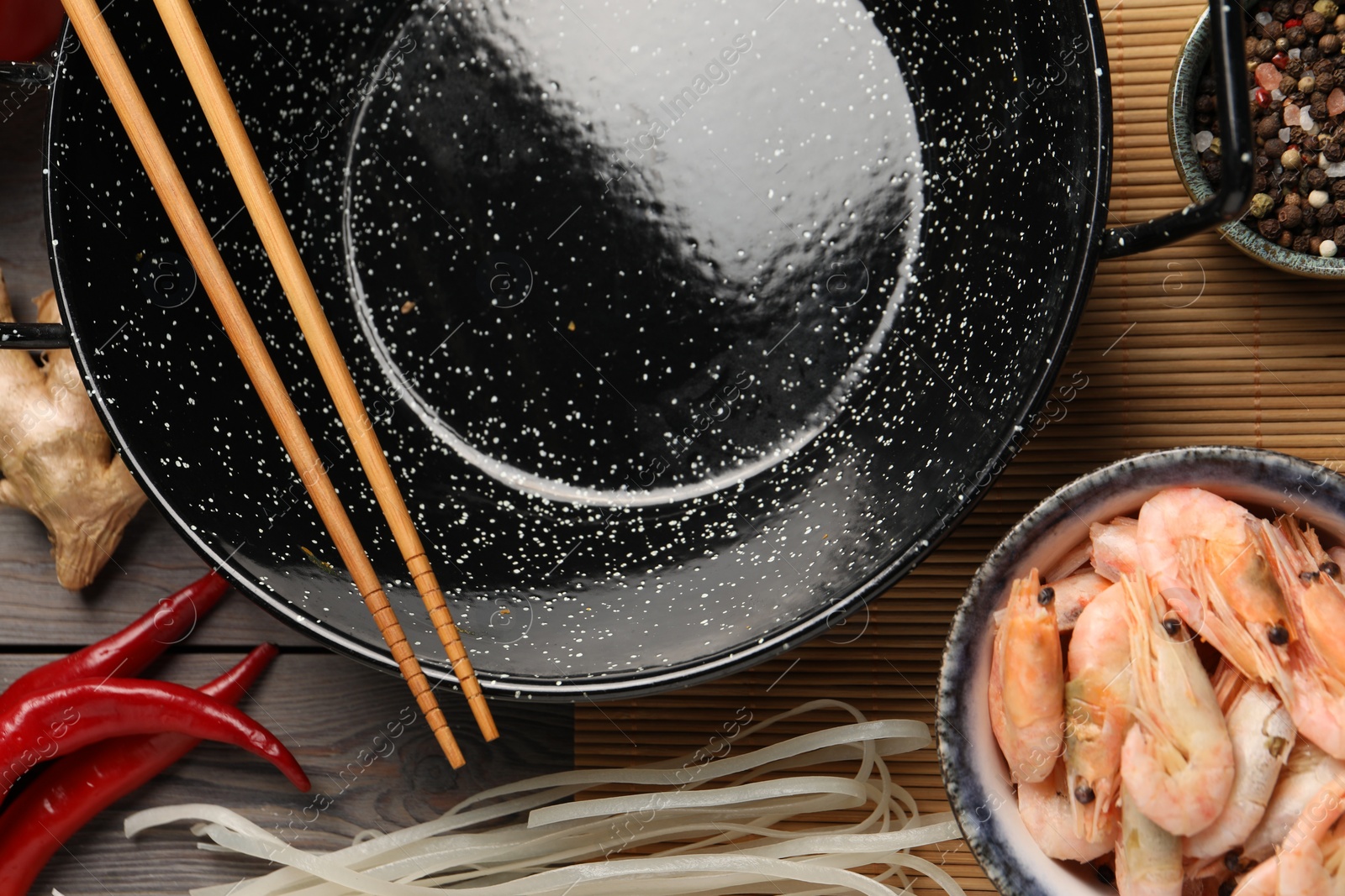 Photo of Black wok, chopsticks and products on color wooden table, flat lay