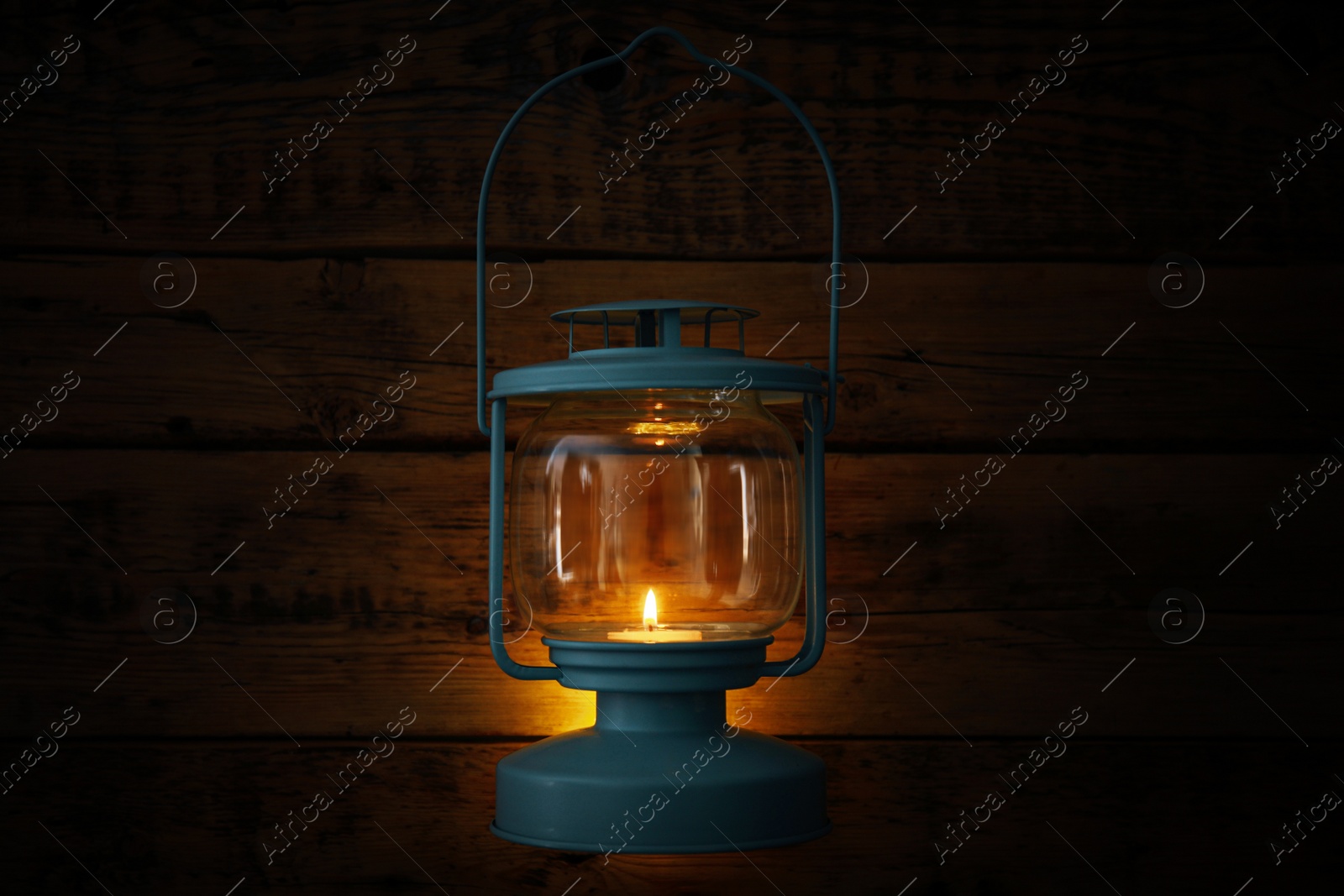 Photo of Vintage lantern with burning candle hanging near wooden wall in darkness