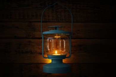 Photo of Vintage lantern with burning candle hanging near wooden wall in darkness